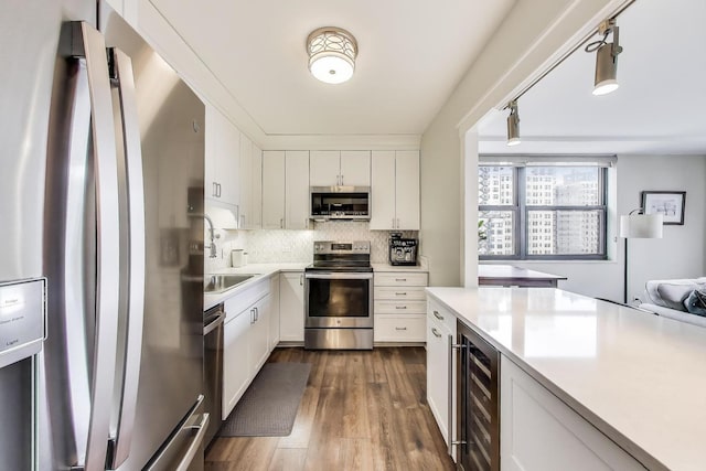 kitchen with a sink, stainless steel appliances, wine cooler, light countertops, and dark wood-style floors