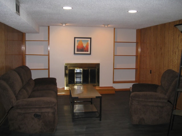living room with wooden walls, a textured ceiling, visible vents, and recessed lighting