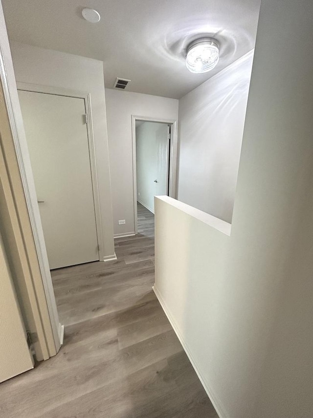 hall featuring baseboards, visible vents, wood finished floors, and an upstairs landing