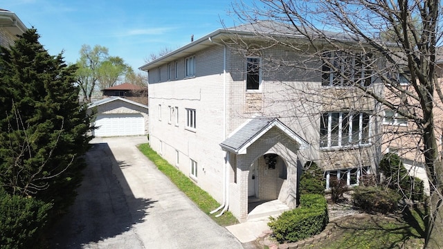 view of front of home featuring a detached garage, brick siding, and an outbuilding