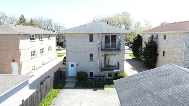 rear view of house with fence, a balcony, and brick siding