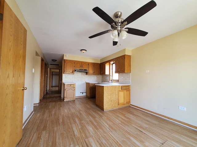 kitchen featuring light countertops, light wood-style flooring, a peninsula, tasteful backsplash, and under cabinet range hood