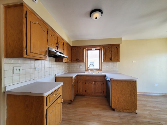 kitchen with brown cabinets, light wood-type flooring, a sink, a peninsula, and under cabinet range hood