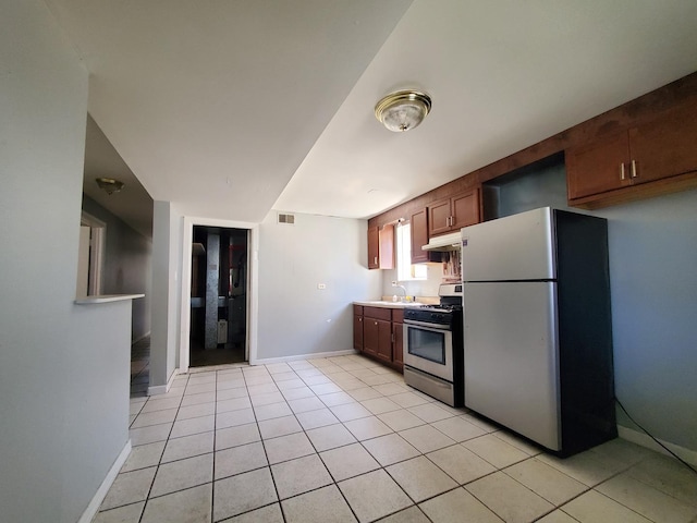 kitchen featuring freestanding refrigerator, baseboards, stainless steel gas range, under cabinet range hood, and a sink