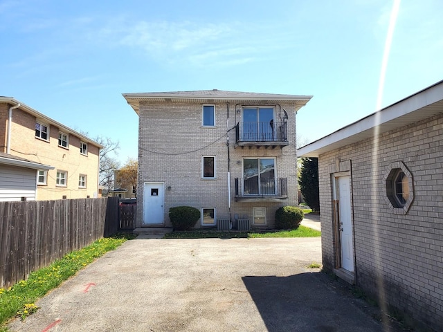 back of property featuring brick siding, fence, a balcony, and cooling unit