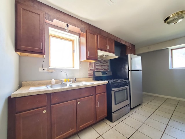 kitchen with appliances with stainless steel finishes, light countertops, light tile patterned floors, a sink, and under cabinet range hood