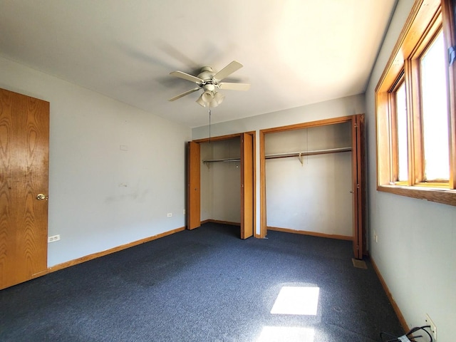 unfurnished bedroom featuring two closets, baseboards, ceiling fan, and dark carpet