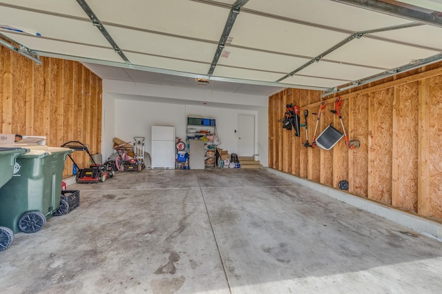 garage with wooden walls, a garage door opener, and freestanding refrigerator