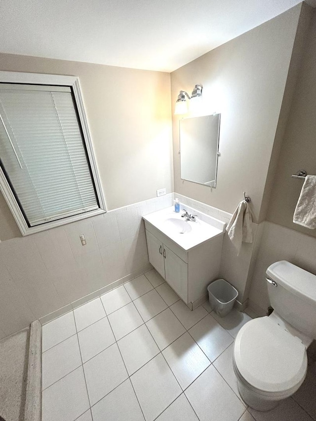 half bath featuring toilet, tile patterned flooring, vanity, and a wainscoted wall
