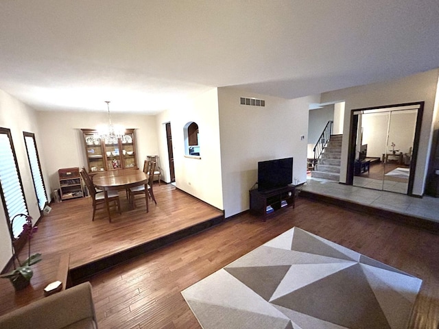 living room with an inviting chandelier, visible vents, wood finished floors, and stairs