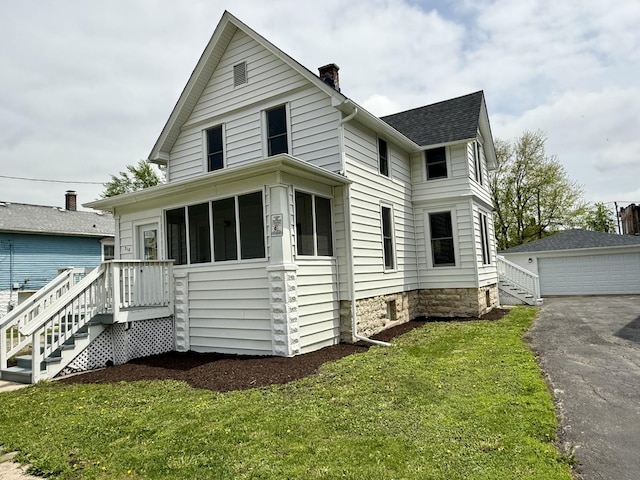 view of front of home with a detached garage, a sunroom, a front yard, an outbuilding, and a chimney