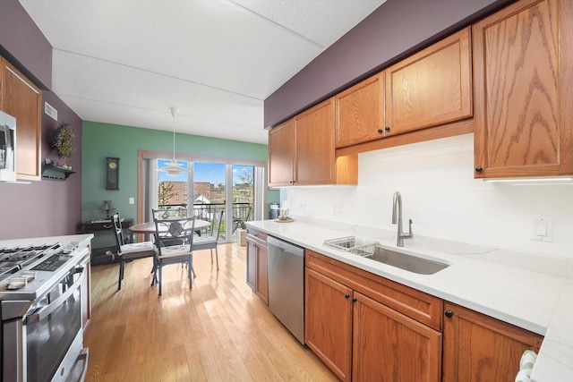 kitchen with a sink, light wood finished floors, light countertops, stainless steel appliances, and decorative backsplash
