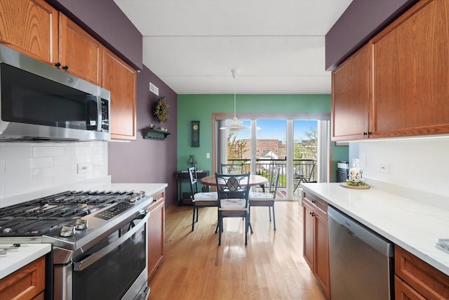 kitchen with brown cabinetry, light wood-style flooring, appliances with stainless steel finishes, and tasteful backsplash