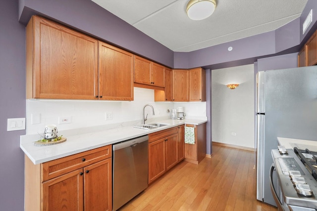 kitchen with appliances with stainless steel finishes, tasteful backsplash, a sink, and light wood-type flooring