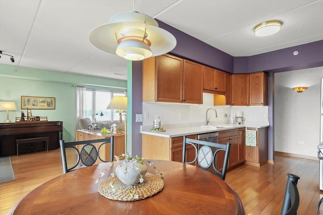 kitchen with brown cabinets, a sink, light countertops, baseboards, and light wood-type flooring