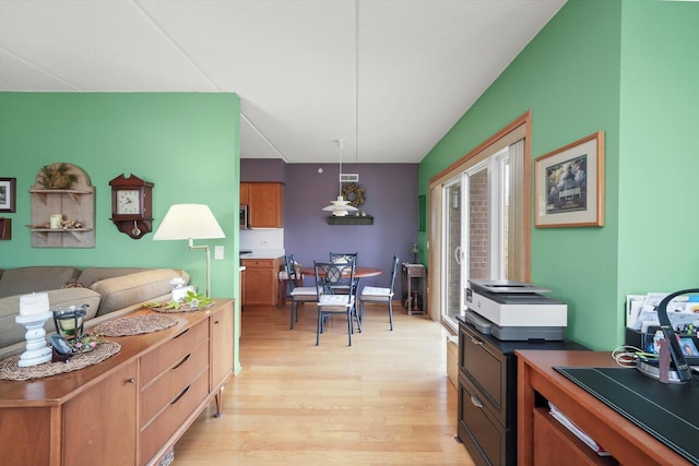 kitchen with stainless steel microwave, hanging light fixtures, brown cabinetry, and light wood-style flooring