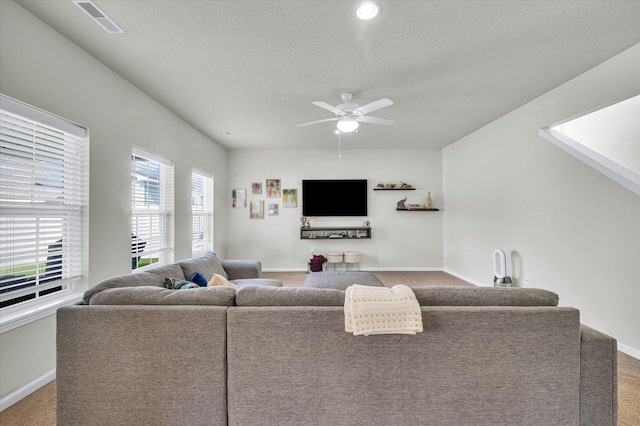 carpeted living area with a ceiling fan, baseboards, and a textured ceiling