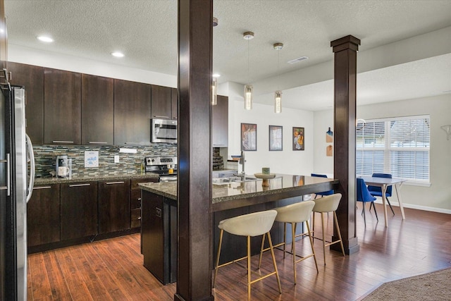 kitchen featuring appliances with stainless steel finishes, a kitchen breakfast bar, dark wood-style floors, decorative backsplash, and a textured ceiling