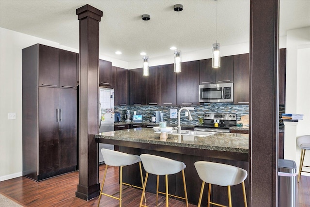 kitchen with appliances with stainless steel finishes, a sink, a kitchen bar, tasteful backsplash, and a textured ceiling