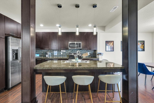 kitchen featuring stainless steel appliances, a sink, a kitchen breakfast bar, dark wood finished floors, and a textured ceiling