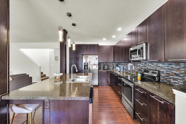 kitchen featuring stainless steel appliances, a sink, a kitchen breakfast bar, tasteful backsplash, and dark wood-style flooring