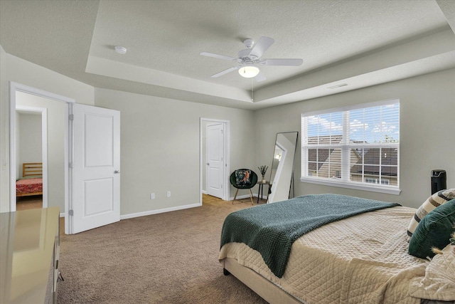 bedroom featuring carpet flooring, a tray ceiling, a textured ceiling, baseboards, and ceiling fan