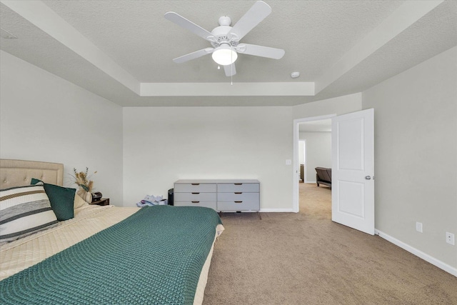 carpeted bedroom featuring a tray ceiling, baseboards, a textured ceiling, and ceiling fan