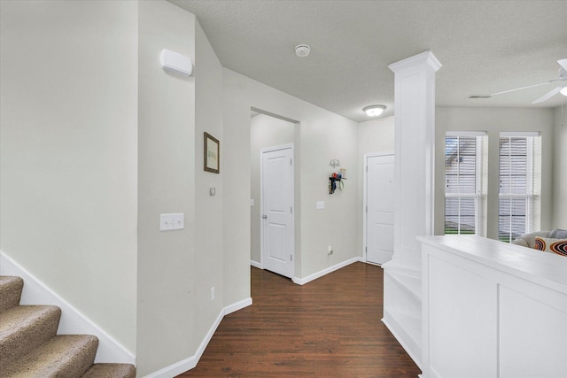 corridor with dark wood-style floors, baseboards, a textured ceiling, stairs, and ornate columns