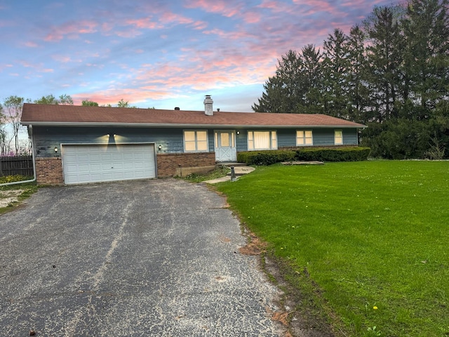 ranch-style home with a front yard, a chimney, brick siding, an attached garage, and driveway