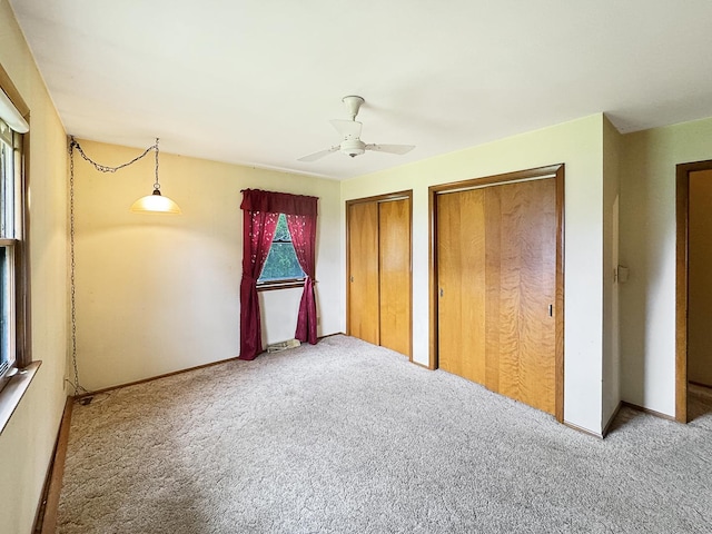 unfurnished bedroom with two closets, ceiling fan, baseboards, and carpet