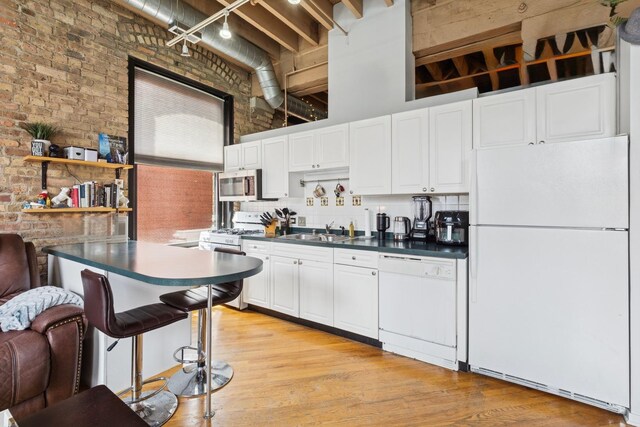 kitchen featuring white appliances, brick wall, dark countertops, and a sink