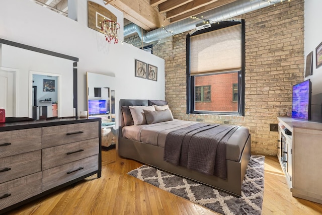 bedroom with light wood-style floors, a high ceiling, and brick wall