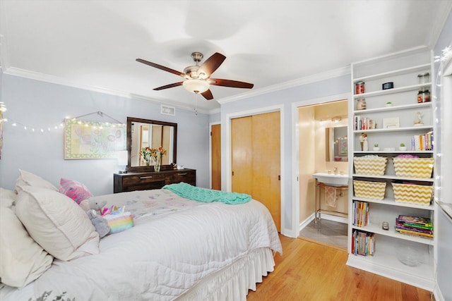 bedroom with wood finished floors, crown molding, ensuite bath, and a ceiling fan