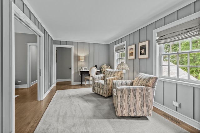 sitting room with a wealth of natural light, a decorative wall, visible vents, and wood finished floors