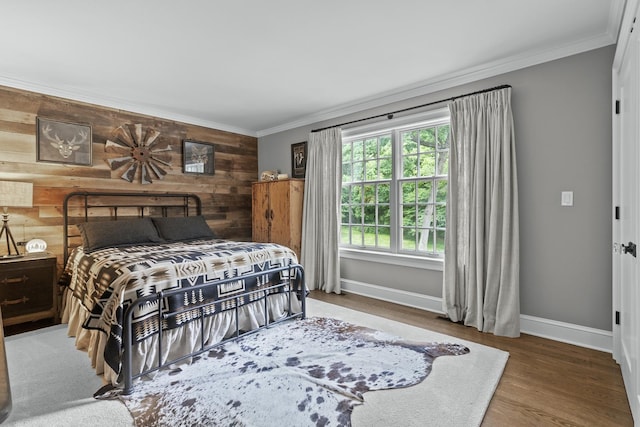 bedroom with crown molding, wood finished floors, wooden walls, and baseboards