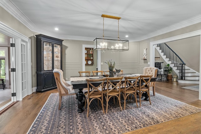dining space featuring stairs, a decorative wall, wood finished floors, crown molding, and a notable chandelier