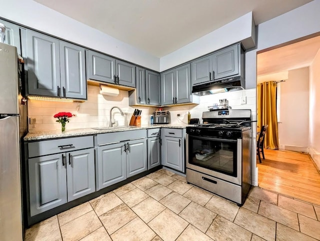 kitchen with decorative backsplash, under cabinet range hood, a sink, gray cabinetry, and stainless steel appliances