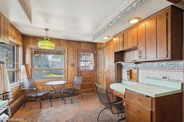interior space with brown cabinetry, wood finished floors, wooden walls, light countertops, and hanging light fixtures