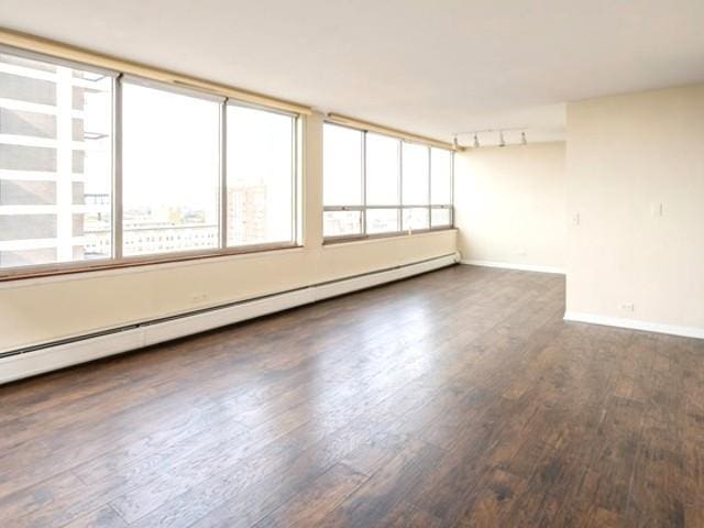 unfurnished room featuring baseboards, plenty of natural light, a baseboard heating unit, and wood finished floors