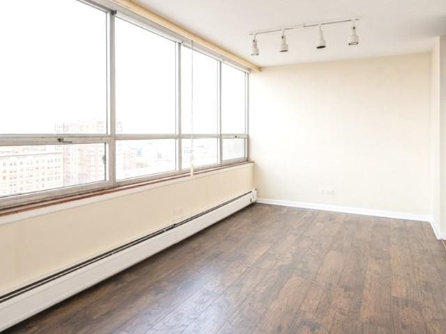spare room with baseboards, track lighting, wood finished floors, and a baseboard radiator