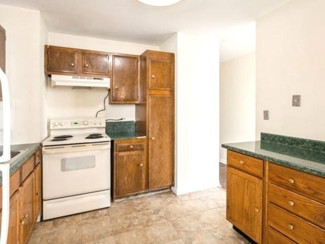 kitchen featuring under cabinet range hood, brown cabinets, dark countertops, and white electric range