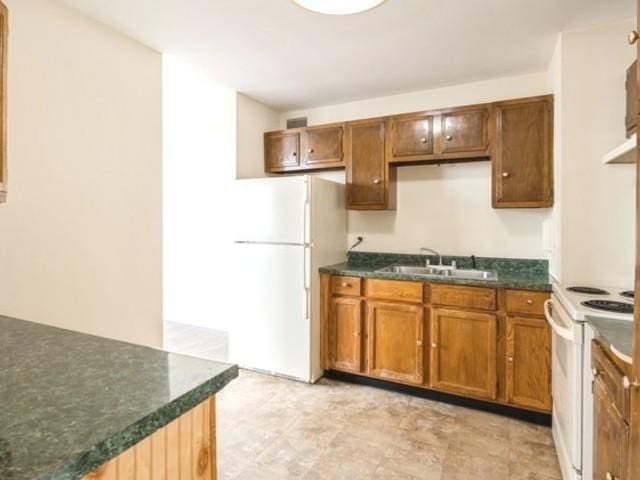 kitchen with a sink, dark countertops, brown cabinetry, and white appliances