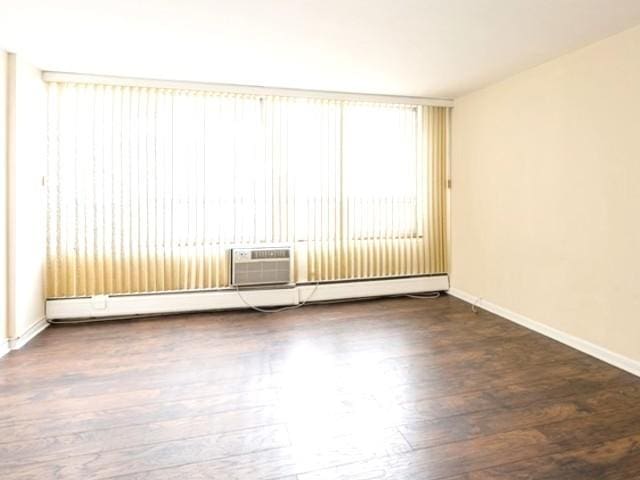 spare room featuring baseboards, a wall unit AC, and wood finished floors