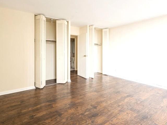 unfurnished bedroom with baseboards, two closets, and wood finished floors