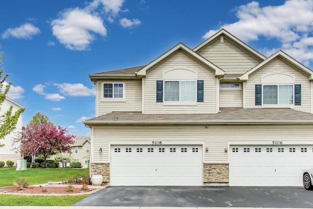 view of front facade featuring an attached garage, driveway, stone siding, and a front yard