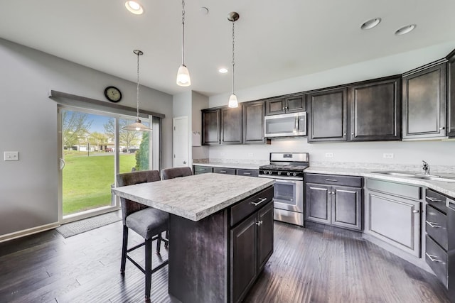 kitchen featuring appliances with stainless steel finishes, a sink, light countertops, a kitchen island, and a kitchen bar