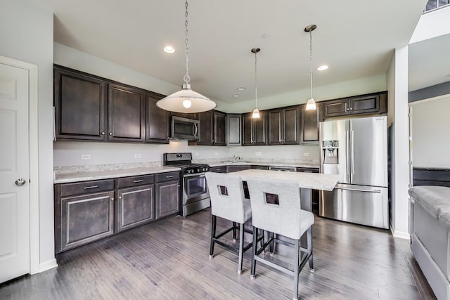 kitchen featuring appliances with stainless steel finishes, dark brown cabinets, light countertops, a breakfast bar, and recessed lighting