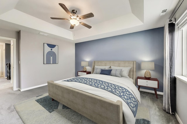 bedroom featuring a raised ceiling, carpet, baseboards, and a ceiling fan