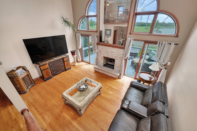 living room featuring a high ceiling, a stone fireplace, and wood finished floors