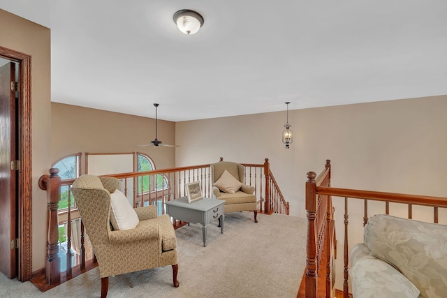 sitting room with a wealth of natural light, carpet, ceiling fan, and an upstairs landing